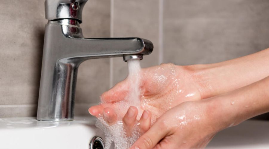Hands washing under a modern faucet with running water, emphasizing plumbing maintenance and hygiene in winter.