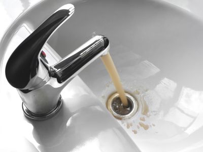 Faucet pouring discolored water into a sink, illustrating potential backflow contamination risks in household plumbing.